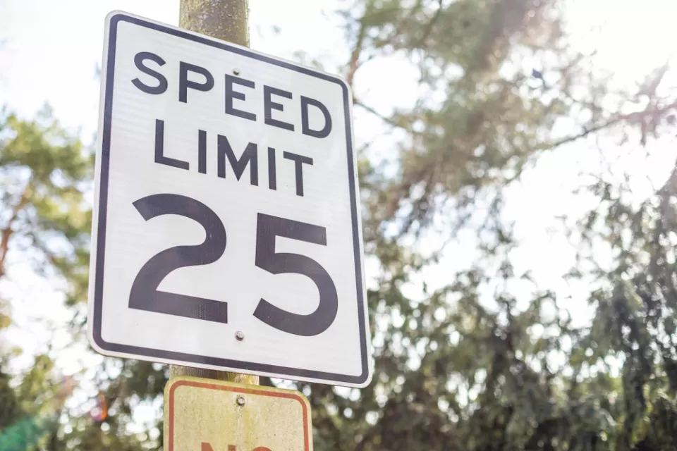 Black and white 25 mph speed limit sign on post with trees in background
